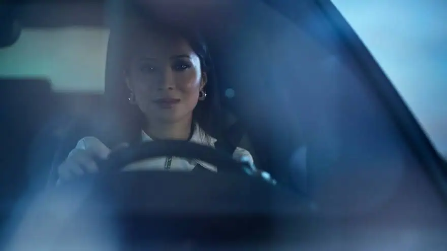 Woman confidently driving a car at night, focused expression, blue lighting.